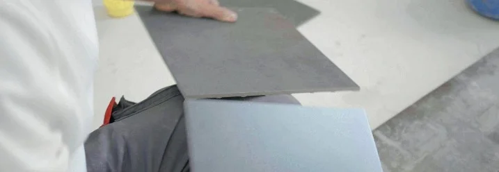 Person hält zwei graue Fliesen.